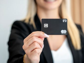 Eine Frau hält eine schwarze Kreditkarte mit VR-Bank Logo und MasterCard Logo in der Hand.