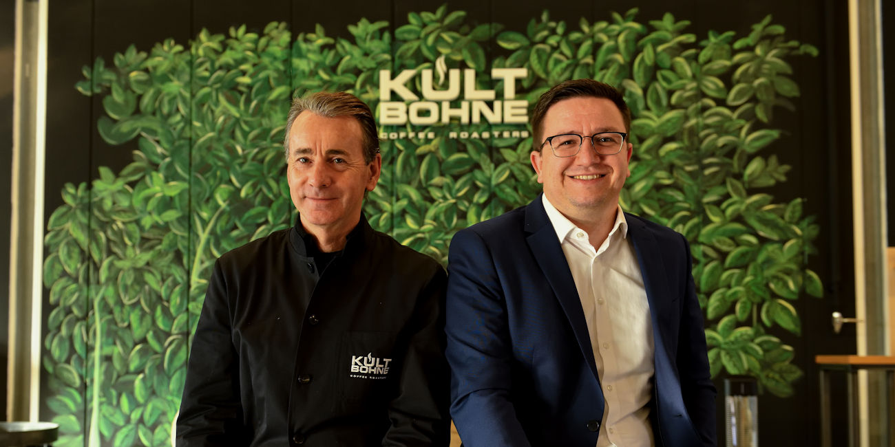 Richard Stetter und Private Banking Berater Julian Bachert vor einer Blätterwand mit dem Logo Kultbohne Coffee Roasters.