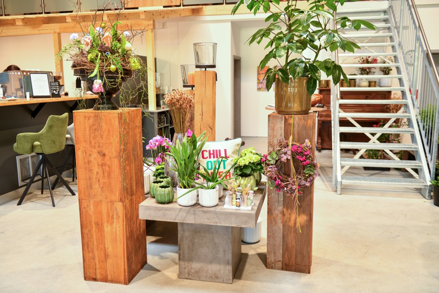 Moderner Verkaufsbereich mit Pflanzen und Blumenarrangements, stilvoll dekoriert mit Holzelementen, im Hintergrund eine Metalltreppe.