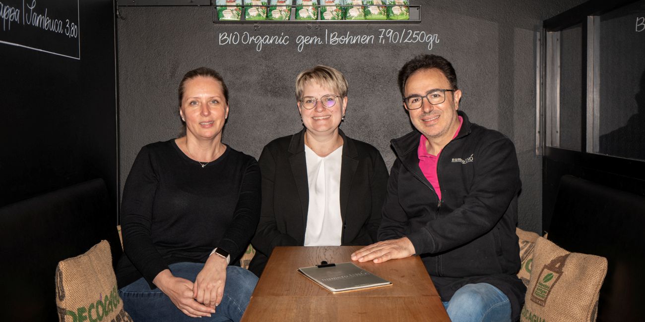 Silke Micello, Private Banking Beraterin Martina Walburger und Antonio Micello sitzen gemeinsam am Tisch im Eiscafe.