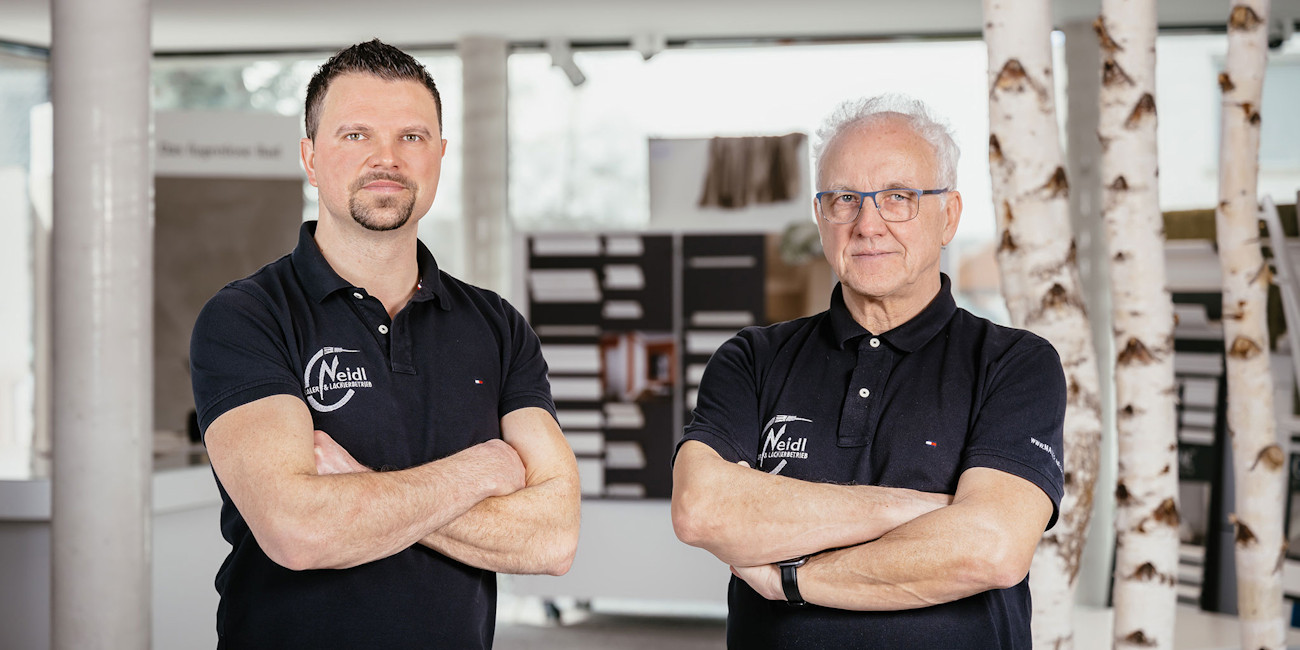 Christian Neidl und sein Vater in den schwarzen Firmen-Shirts mit Logo im Ausstellungsraum.