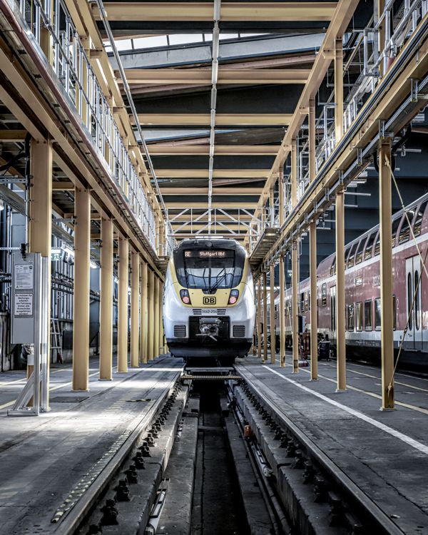 Auf einer Baustelle steht ein mobiles Rollgerüst zwischen Betonpfeilern – zwei Handwerker arbeiten in luftiger Höhe daran.