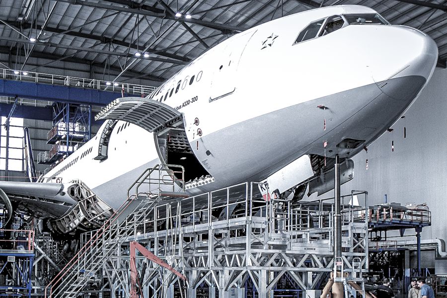 Eine große Testkammer mit komplexem Leiter- und Plattformsystem, in der ein Mitarbeiter im Schutzanzug an einer Anlage arbeitet.