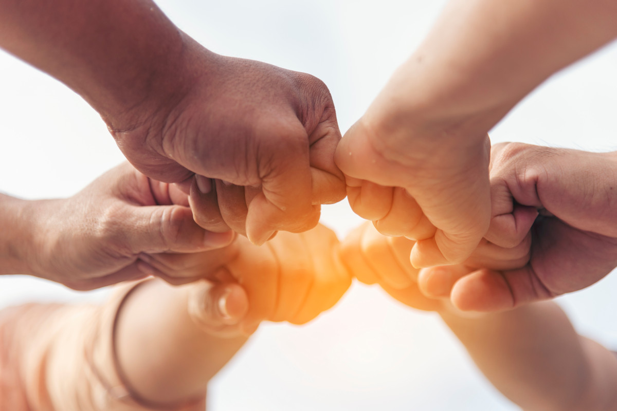 5 unterschiedliche Menschen halten ihre Fäuste zusammen.