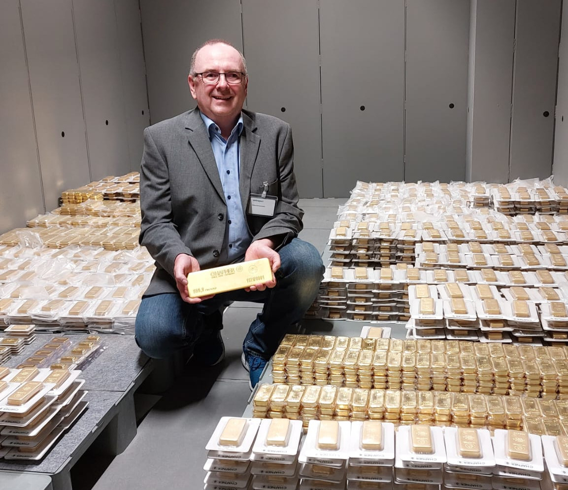 Berater Private Banking Alwin Renner kniet im Tresorraum und hält einen großen Goldbarren in der Hand. Um ihn herum sind zahlreiche weitere Goldbarren.